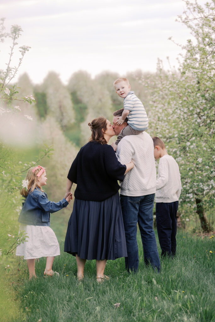 The Potter Family  holding hand walking through an apple farm. Their youngest son is on Dad's shoulders.