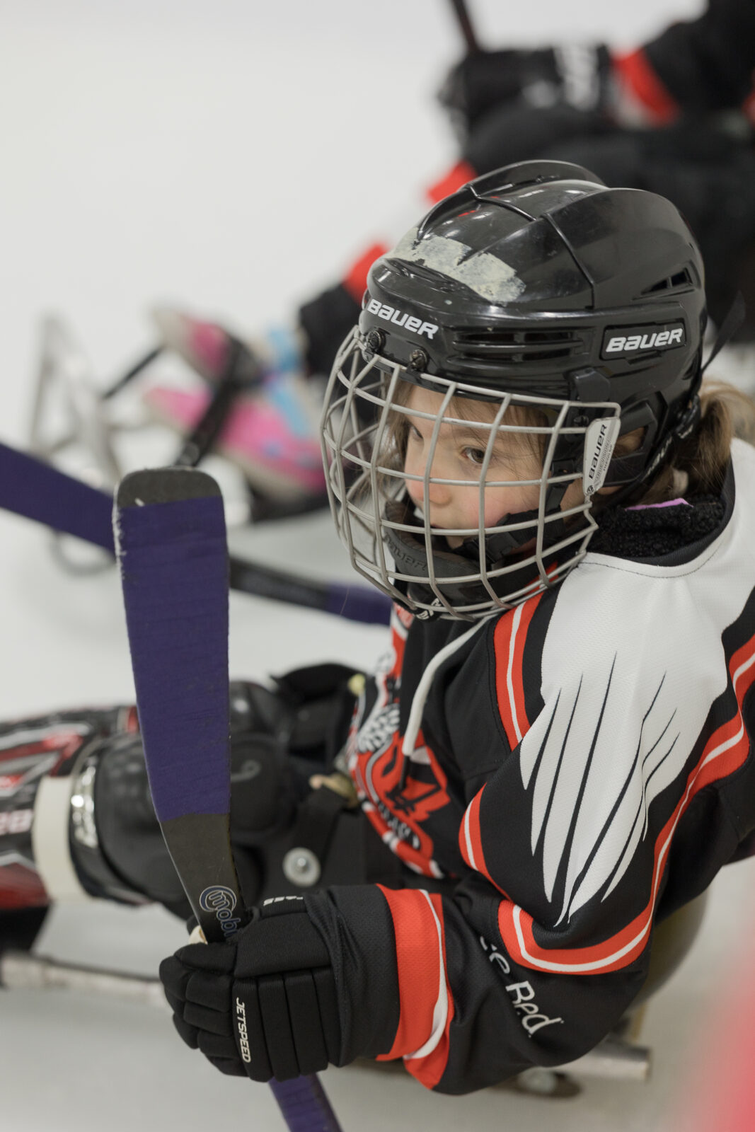 An image of Dahlia wearing her Sledwings gear while holding her purple taped hockey stick