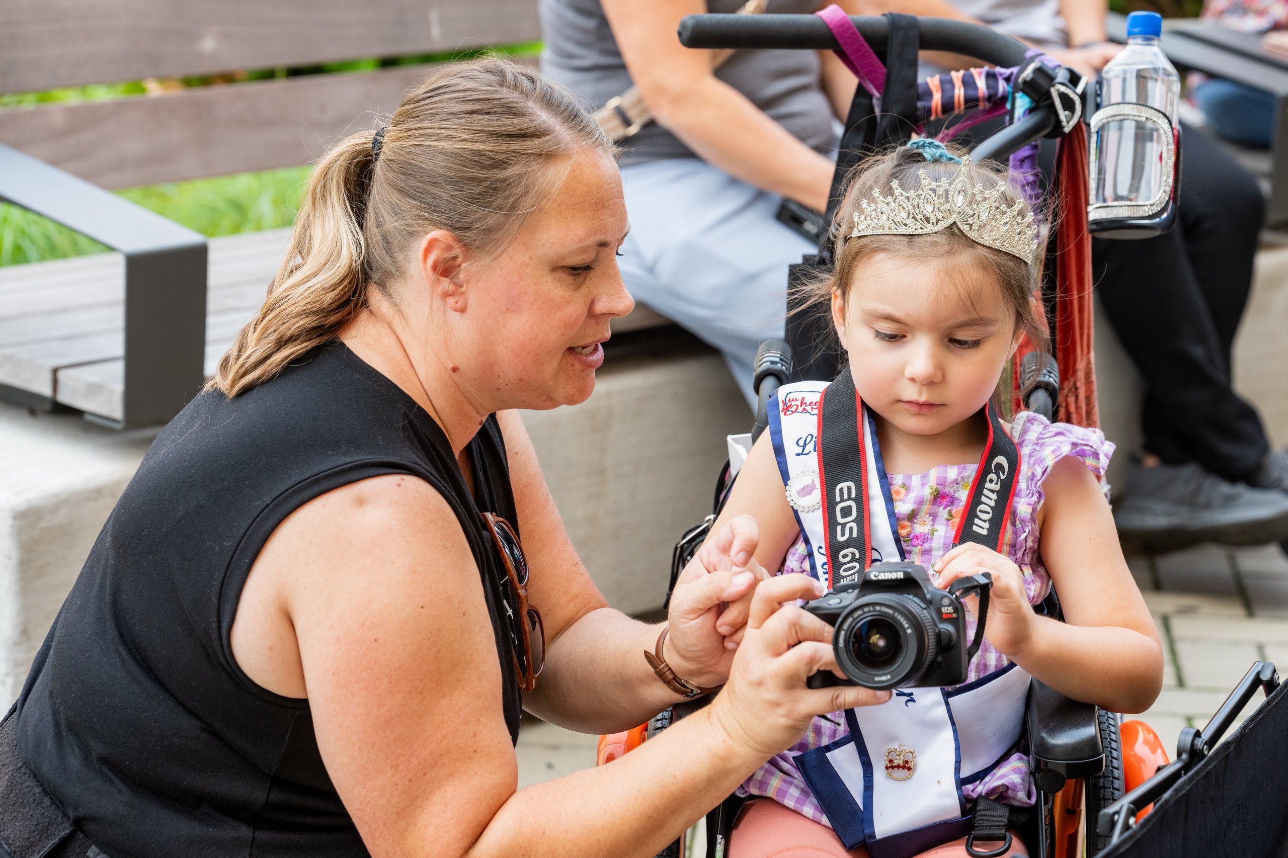 Little Ms. Wheelchair America Dahlia Swanson, seated in her wheelchair, learning to use a camera with a Hopelynd photographer