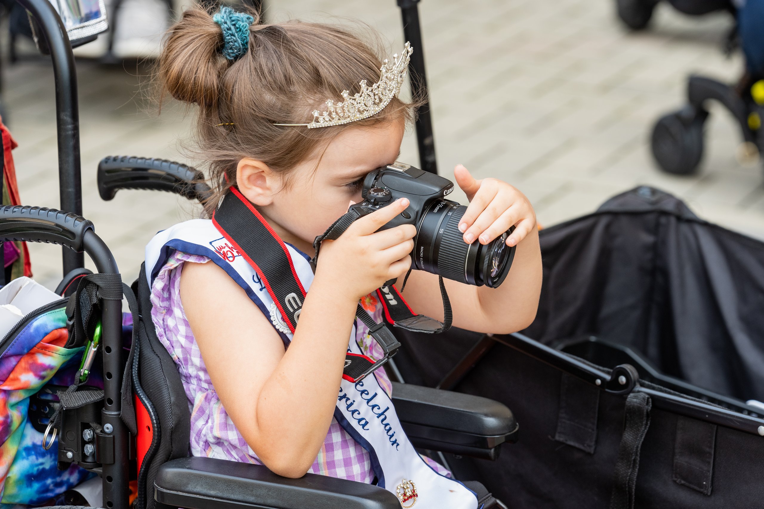 Little Ms. Wheelchair America Dahlia Swanson looking through a camera viewfinder from her wheelchair during the Walk and Roll