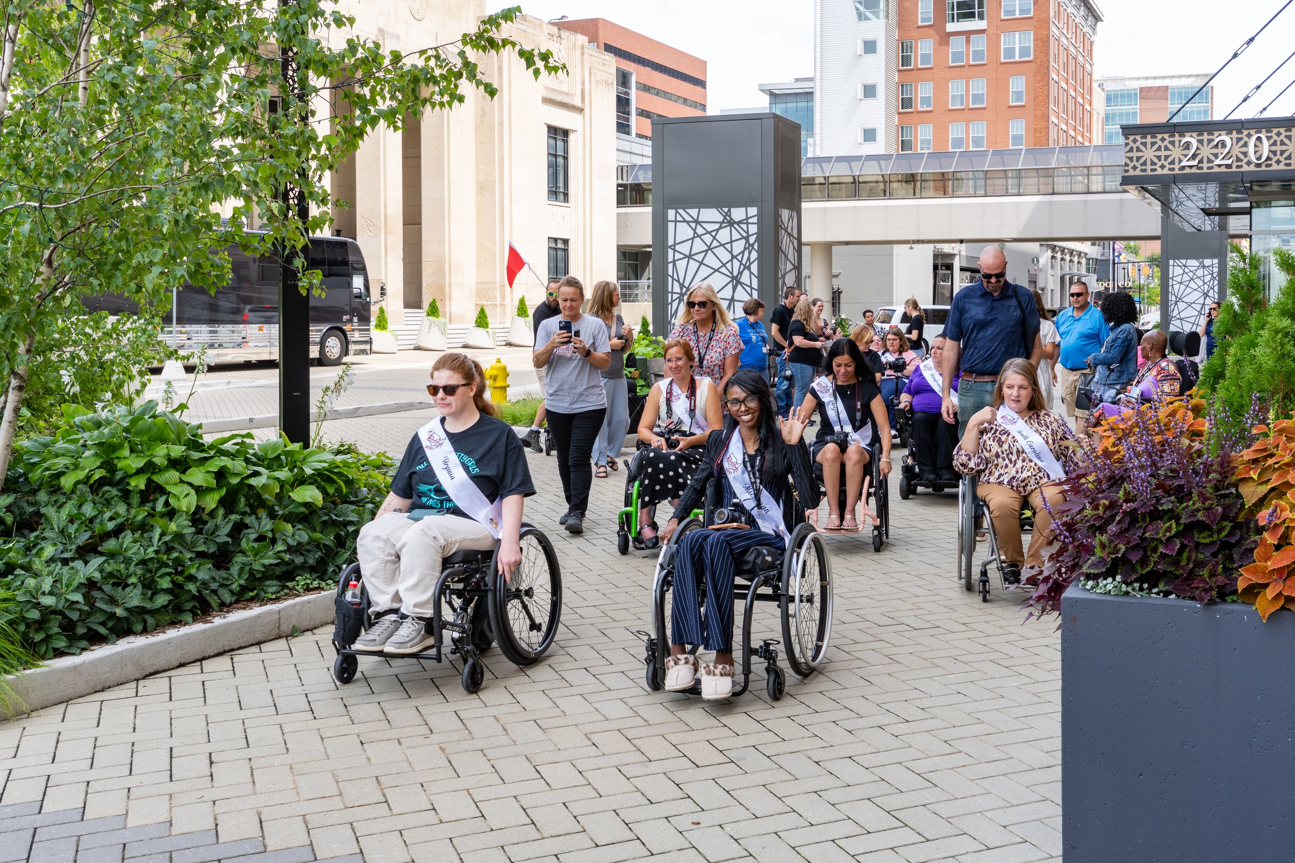Ms. Wheelchair America delegates rolling in their wheelchairs along a downtown Grand Rapids sidewalk during the Hopelynd Walk and Roll
