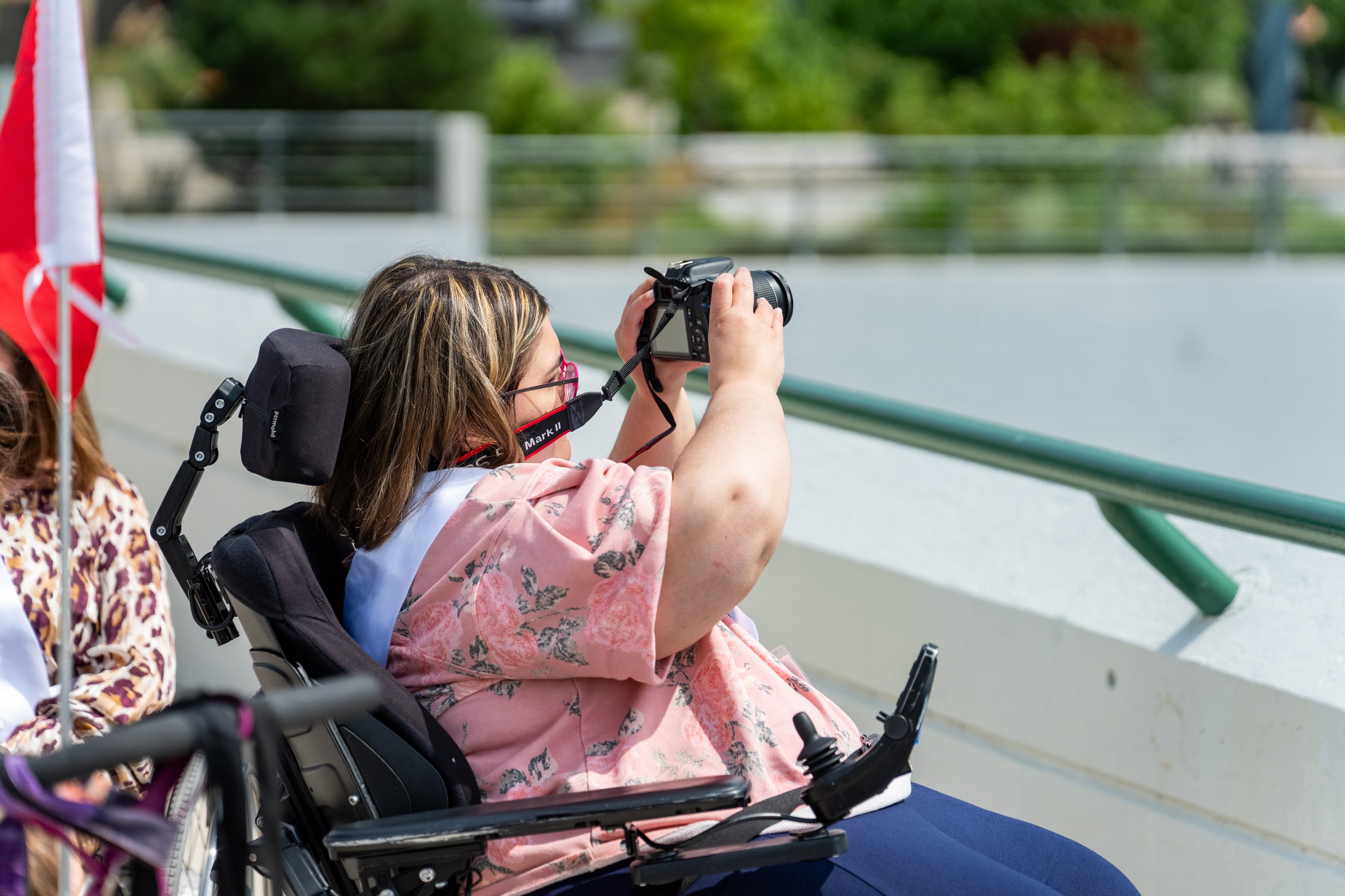 A Ms. Wheelchair America delegate in a power wheelchair taking a photo along the Grand River in downtown Grand Rapids