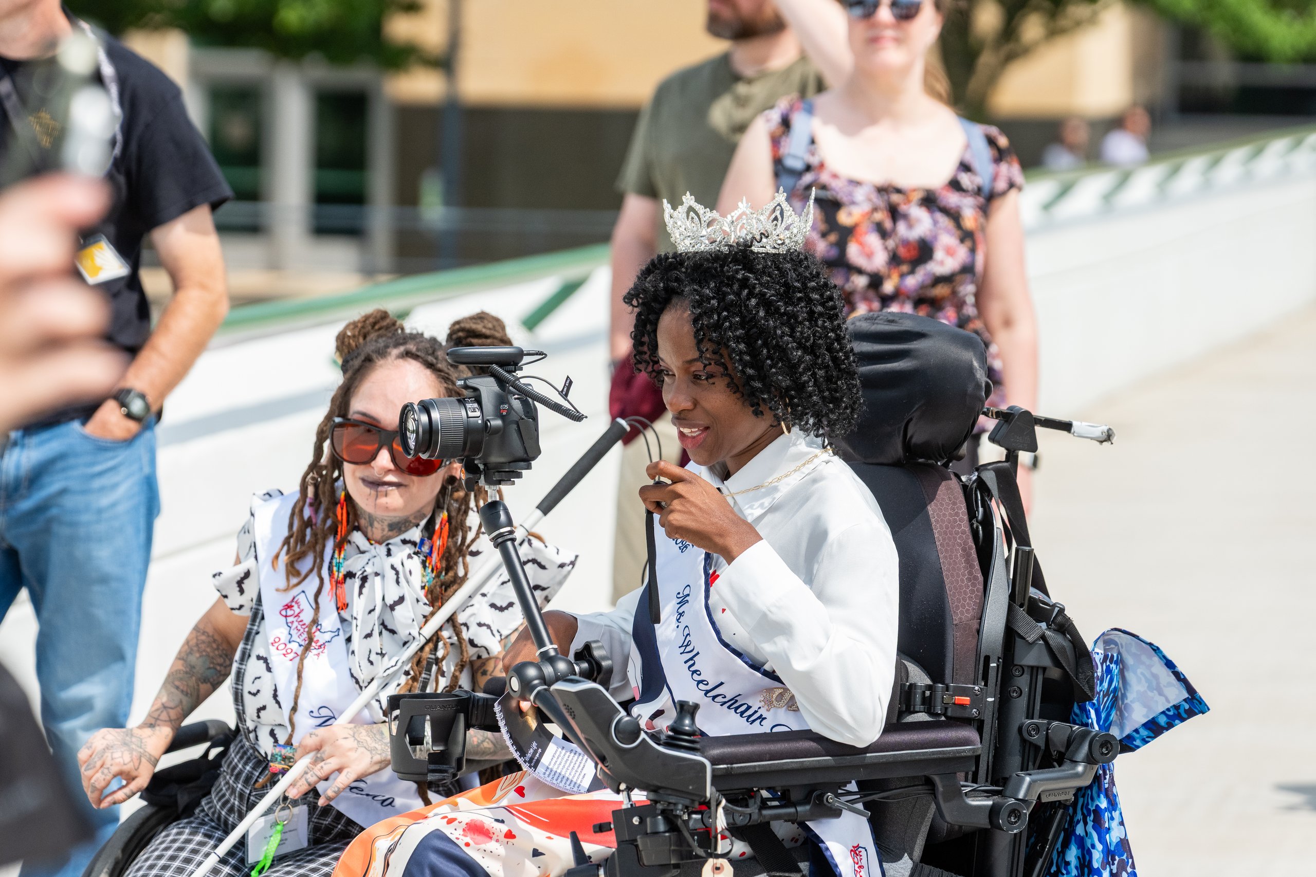 Two Ms. Wheelchair America delegates in wheelchairs taking photos with their cameras during the Walk and Roll in Grand Rapids