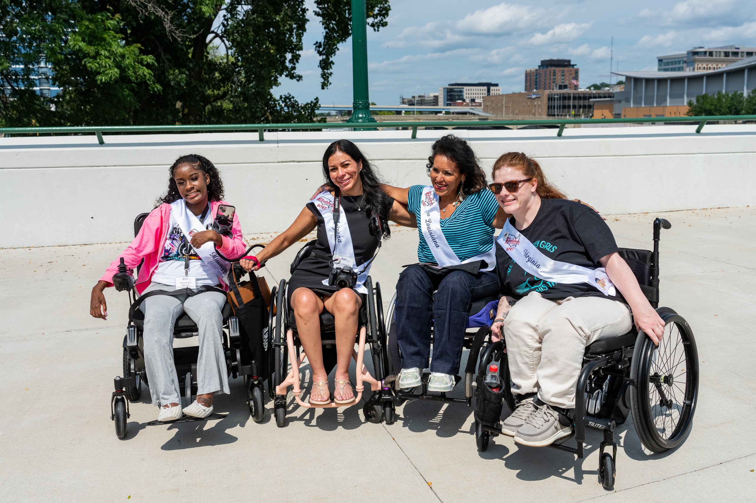 Four Ms. Wheelchair America delegates in wheelchairs laughing together on a Grand Rapids plaza