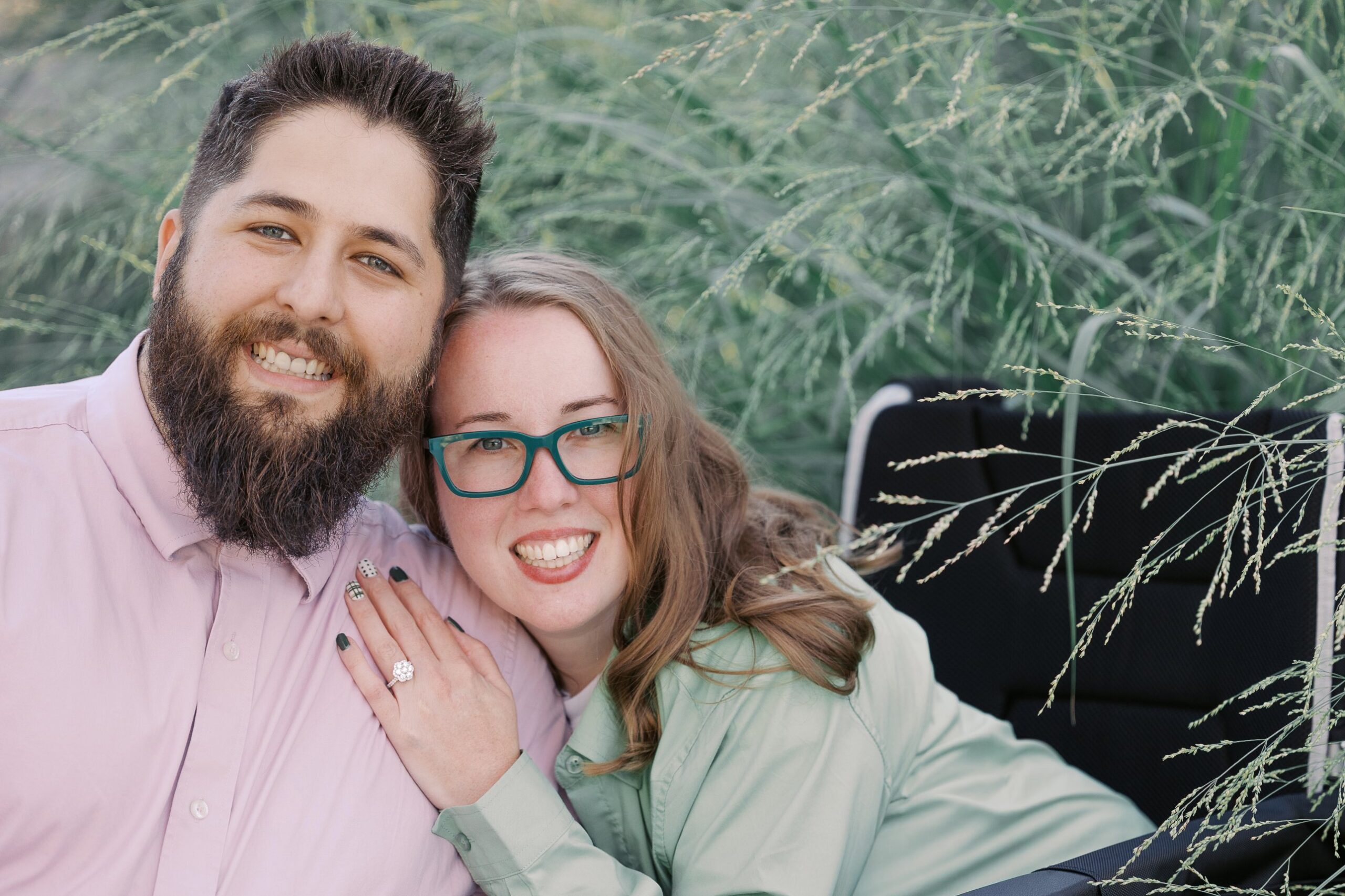 Katie, a powerchair user, and Saleem smiling at the camera with her engagement ring on his shoulder