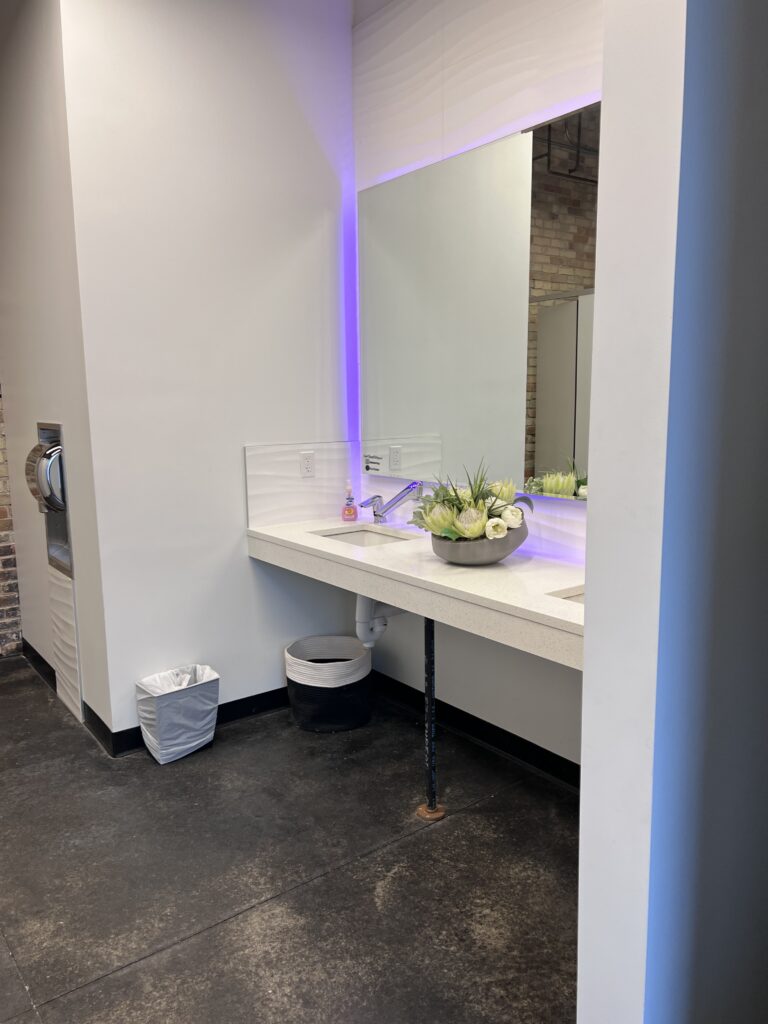 Restroom sink counter with open space underneath and a lighted mirror