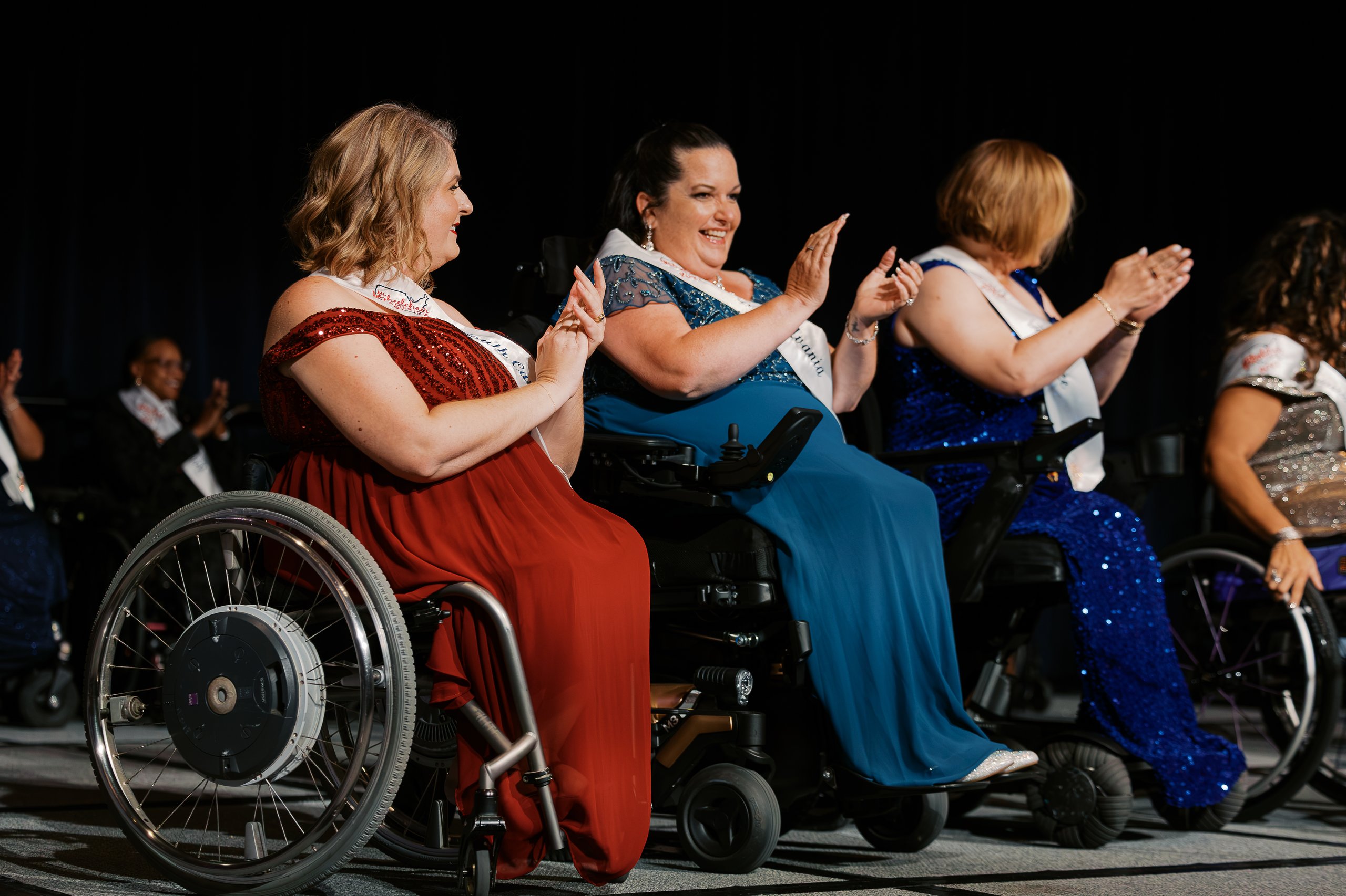 Ms. Wheelchair America delegates in wheelchairs and evening gowns applauding on stage