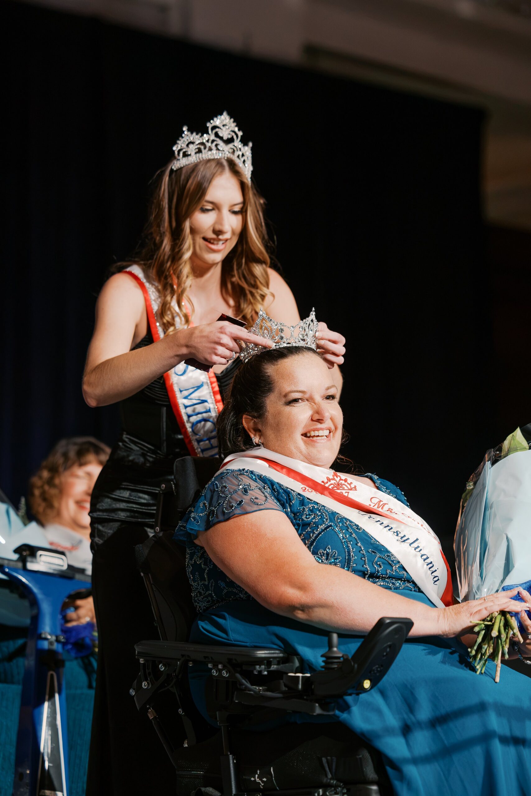 The crown is placed on Jamie Clendening, Ms. Wheelchair America 2027, seated in her power wheelchair holding flowers