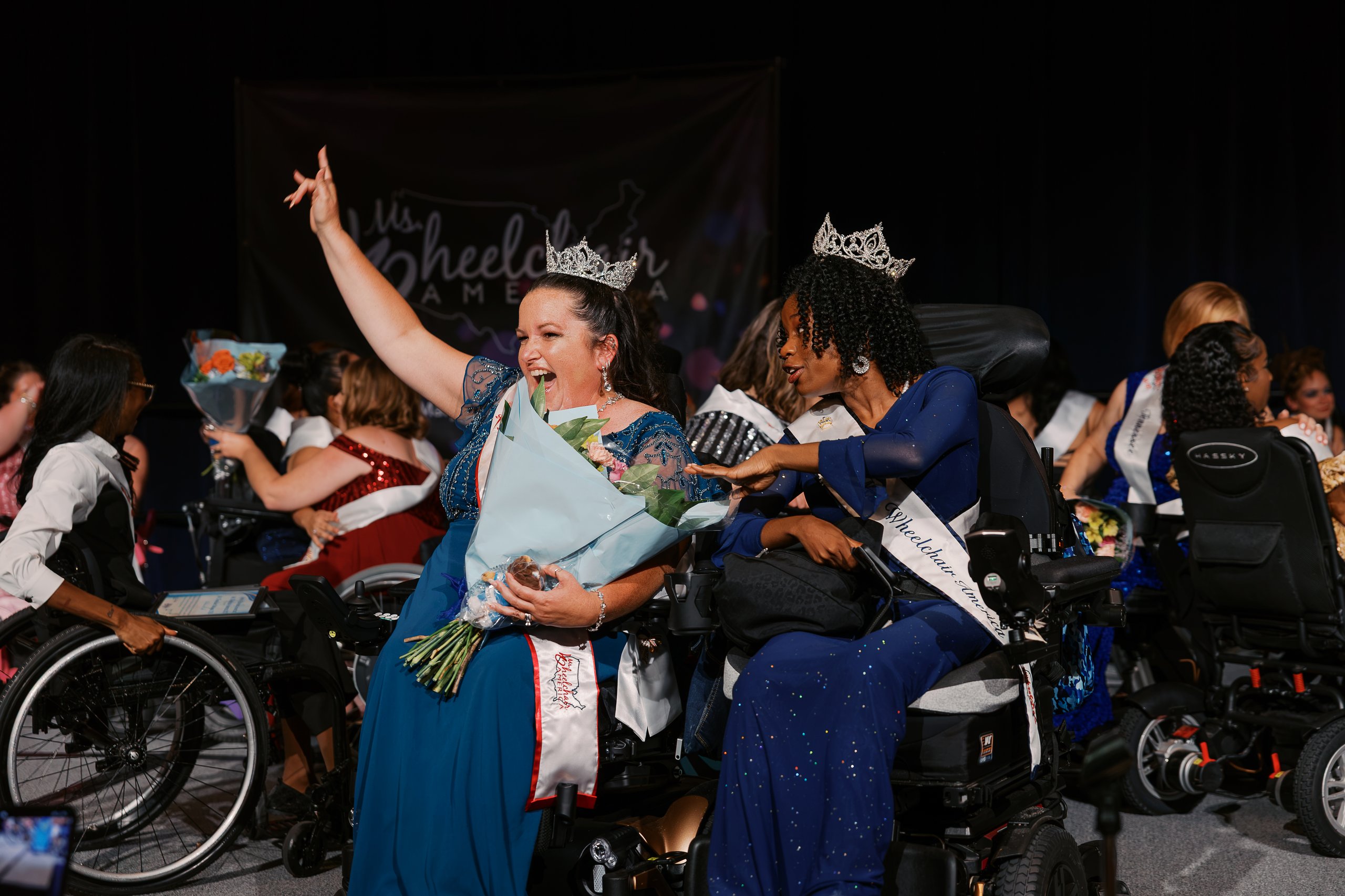 Jamie Clendening raising her hand in celebration, surrounded by fellow Ms. Wheelchair America delegates in wheelchairs