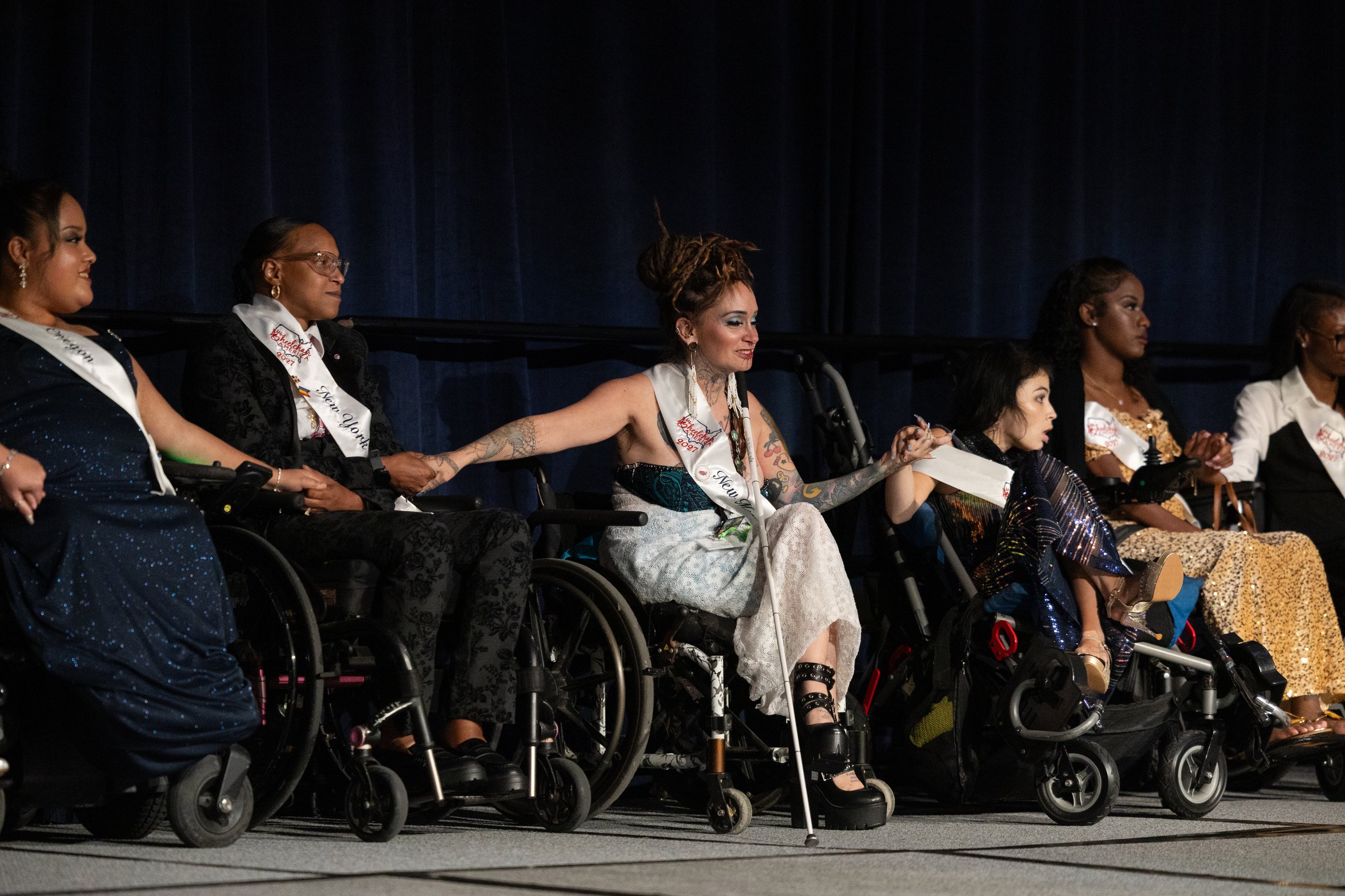 Ms. Wheelchair America 2027 delegates in wheelchairs lined up on stage holding hands during the crowning ceremony