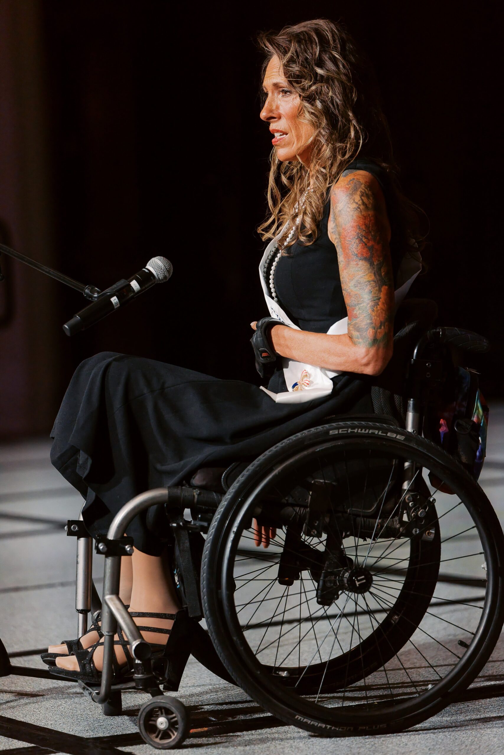 A delegate in a manual wheelchair speaking into the microphone at Ms. Wheelchair America Speech Night