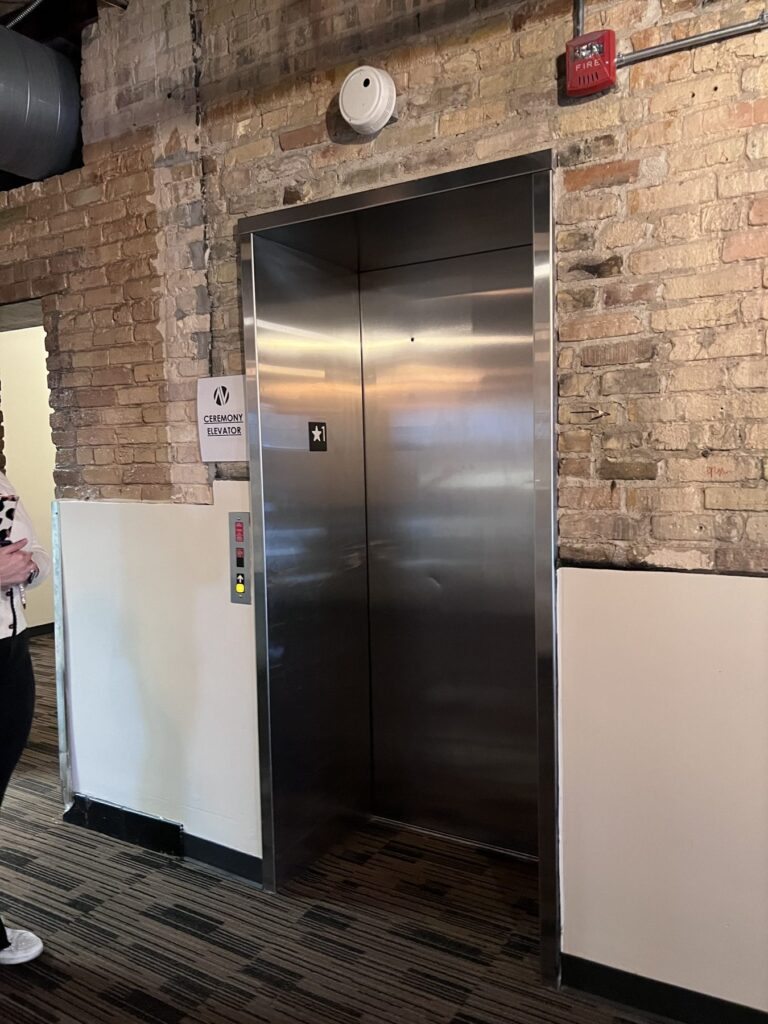 A stainless steel elevator on the main floor of New Vintage Place, with a sign reading "Ceremony Elevator."