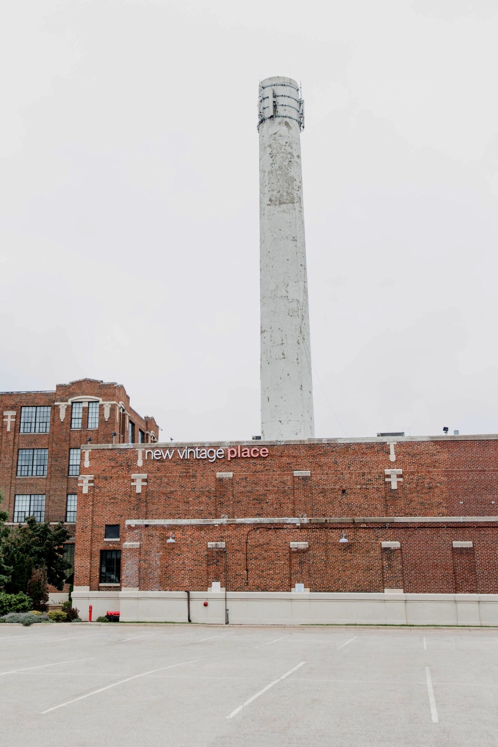 The brick exterior of New Vintage Place with its sign and the tall white historic smokestack, seen from the parking lot.