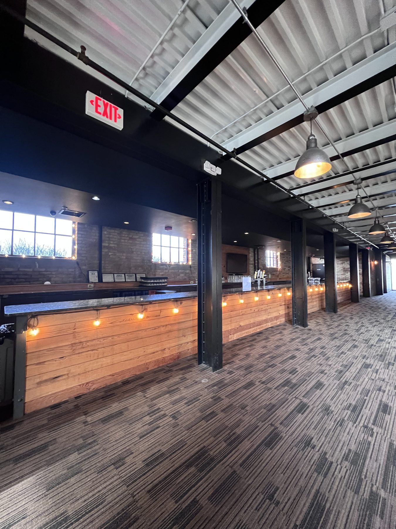 The long wood-front bar in the cocktail lounge, with a wide carpeted walkway alongside it.