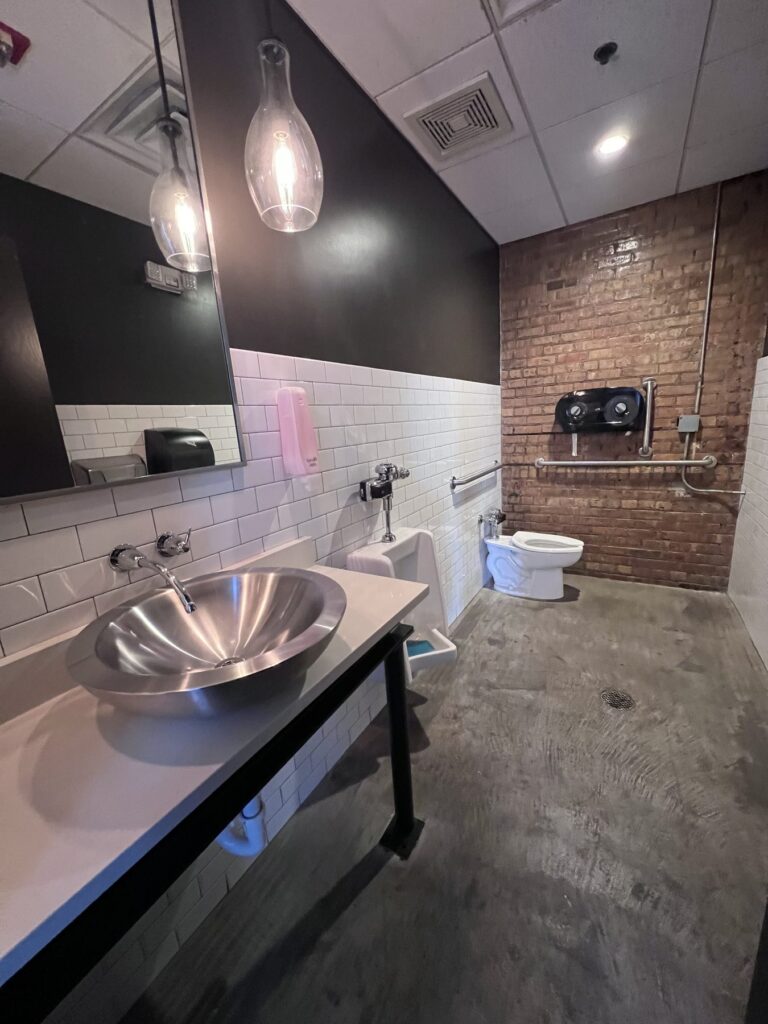 A restroom with a sink counter that is open underneath and a grab bar behind the toilet.