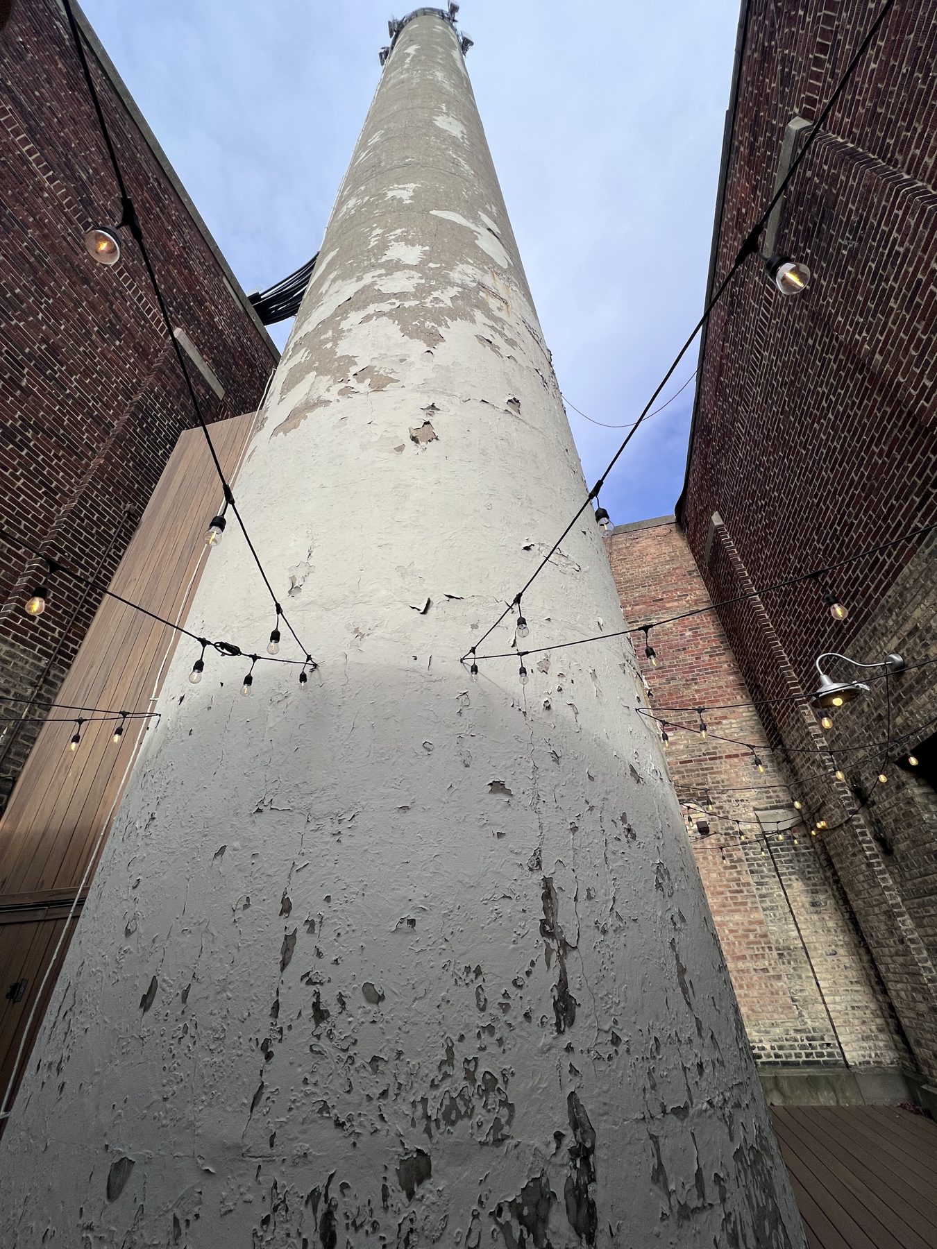 The historic smokestack on the Stack Patio, with string lights overhead between brick walls.