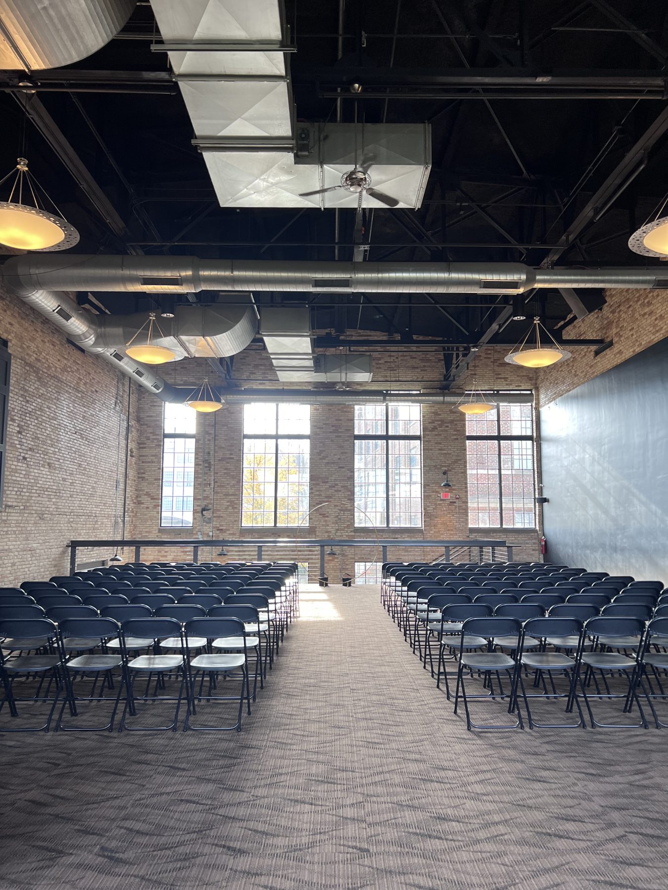 Vintage Hall set for a ceremony, with rows of black chairs on each side of a wide center aisle and tall windows at the front.