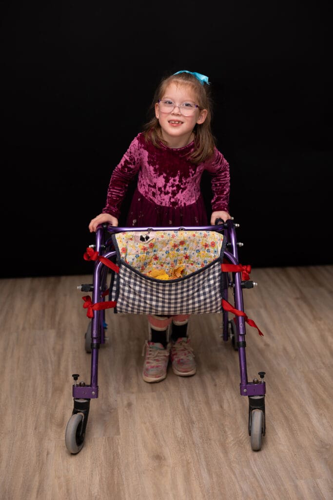 Young girl smiling while standing with a purple walker during a fall family photo session at the Children’s Healing Center of West Michigan.
