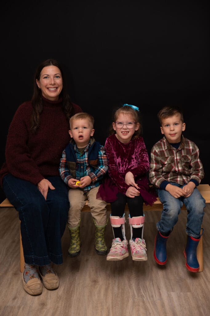 Parent sitting with three children on a bench during a fall family photo session at the Children’s Healing Center of West Michigan.